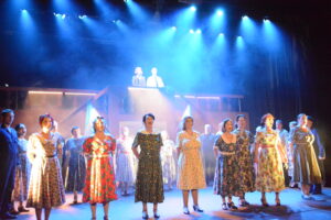Home A group of people standing on stage in 1940s costumes