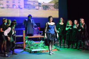 Home A woman in a blue dress surrounded by other women dressed in black and green steampunk style
